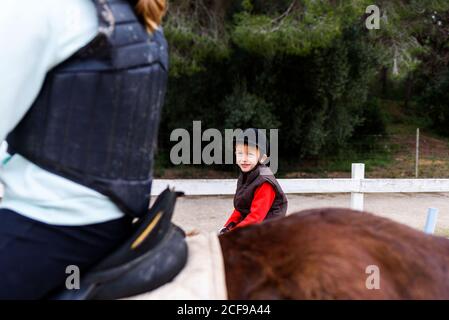ragazzo su pony roan e ragazza anonima su cavalli marroni cavallo su dressage arena durante la lezione in scuola equestre Foto Stock