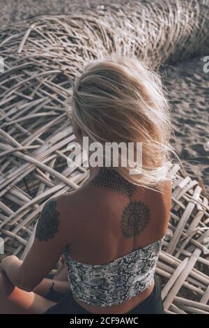 Allegro giovane biondo che indossa abiti estivi casual con tatuaggi le spalle poggiano sui sedili in vimini mentre si guarda al sole giorno d'estate Foto Stock