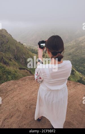 Dall'alto di Donna in vestito bianco che prende colpo di maestose montagne verdi nella foschia in piedi sull'alta cima in Sri Lanka Asia Foto Stock