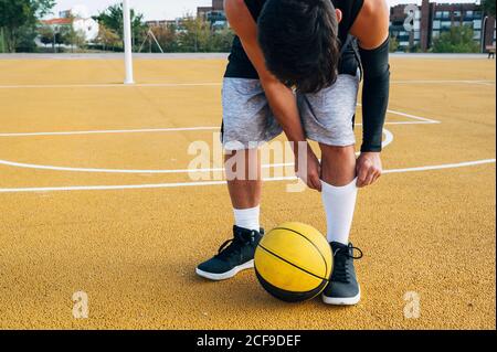 Gambe di raccolto giovane uomo e palla che gioca a basket corte all'aperto che fissa la sua calza Foto Stock
