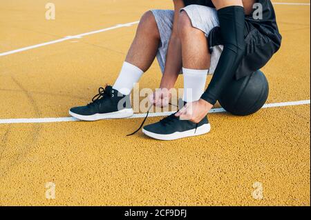 Gambe di raccolto giovane uomo e palla seduta sul basket corte all'aperto che fissa la sua calza Foto Stock