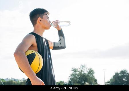 Giovane uomo che gioca sul campo di pallacanestro giallo acqua potabile all'aperto Foto Stock