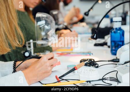 Vista laterale della studentessa di raccolto seduta al tavolo e. lavorare con dental bur mentre studia odontoiatria in classe moderna Foto Stock