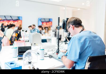 Vista posteriore dello studente di odontoiatria maschile in uniforme e guanti lavorare con il microscopio mentre si esegue un'operazione dentale in una moderna classe Foto Stock