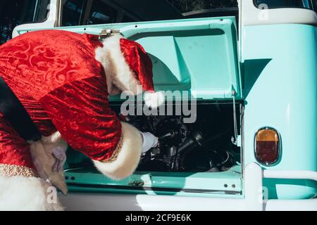 Persona irriconoscibile in costume rosso e bianco di Babbo Natale ispezione del motore del pulmino verde d'epoca in giornata di sole Foto Stock