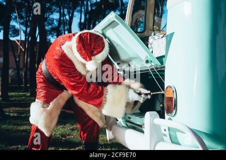 Persona in costume rosso e bianco di ispezione di Babbo Natale motore di vintage van verde in giornata di sole Foto Stock