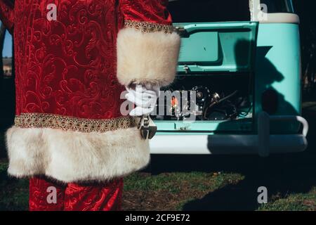 Persona irriconoscibile in costume rosso e bianco di Babbo Natale ispezione del motore del pulmino verde d'epoca in giornata di sole Foto Stock