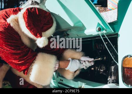 Persona irriconoscibile in costume rosso e bianco di Babbo Natale ispezione del motore del pulmino verde d'epoca in giornata di sole Foto Stock