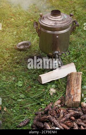 Riscaldamento del samovar con coni per la preparazione del tè. Il samovar si trova sull'erba. Fumo dal tubo Foto Stock