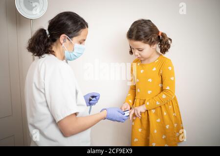 Un medico in guanti di lattice utilizzando il bracciale per le dita per l'esame pressione sanguigna della bambina in abito casual giallo Foto Stock