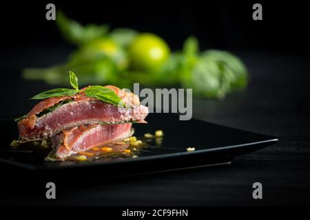 Tonno rosso profumato e succoso con prosciutto al basilico e merletto di pollo sulla piastra nera Foto Stock