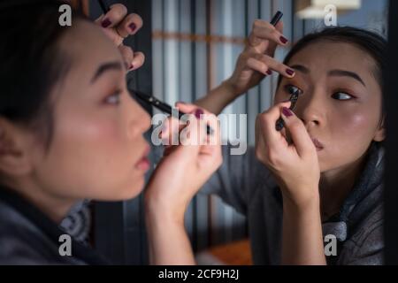 Donna asiatica applicazione eyeliner di fronte allo specchio Foto Stock