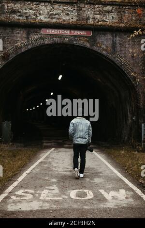 uomo che cammina di fronte al tunnel scuro sulla strada Foto Stock