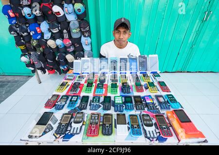 Dili, Timor Est - 09 AGOSTO 2018: Giovane fornitore asiatico maschio che vende dispositivi elettronici e tappi sulla strada della città Foto Stock