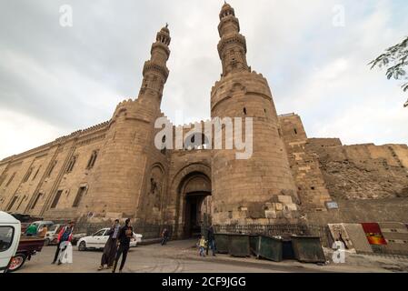 Cairo, Egitto - 14 dicembre 2019: Persone che camminano sulla vecchia strada contro vecchio castello di pietra con arco e torri Foto Stock