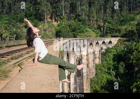 Donna asiatica rilassata seduta sul ponte gambe penzolanti e mano ondulata Foto Stock