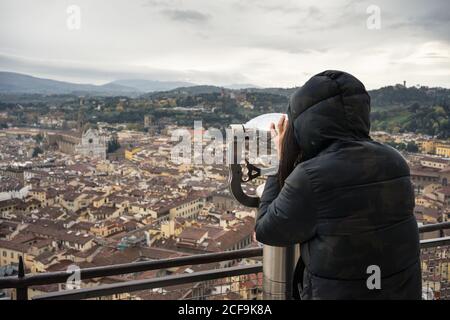 Vista posteriore dell'anonima donna che utilizza binocoli per esplorare le antiche strade di Firenze mentre si trova sulla piattaforma di osservazione vicino alla cupola del Brunelleschi in Italia Foto Stock
