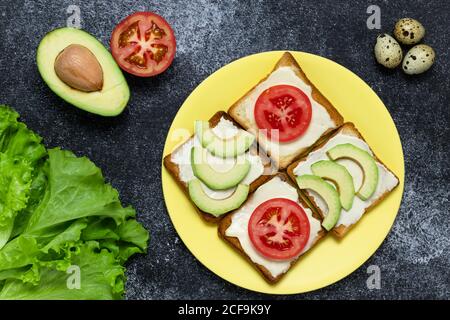 Panini con avocado e pomodori su sfondo scuro. Foglie di lattuga e uova di quaglia su una tavola nera. Concetto di cibo sano, vita morta. Crostini Foto Stock