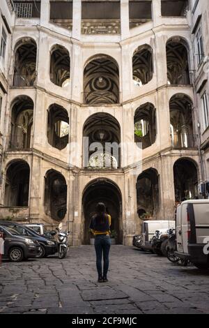 Vista posteriore di una donna di riposo irriconoscibile in piedi su strada acciottolata E visita al bellissimo palazzo storico dello Spagnolo A Napoli in Italia Foto Stock