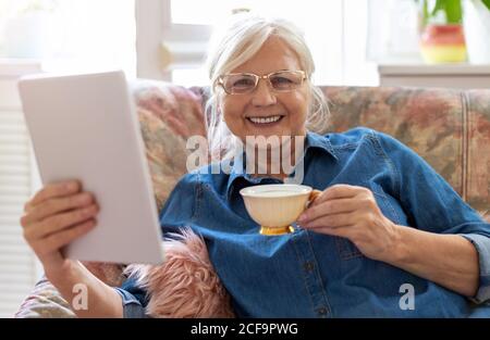 Donna senior con tavoletta digitale in casa Foto Stock