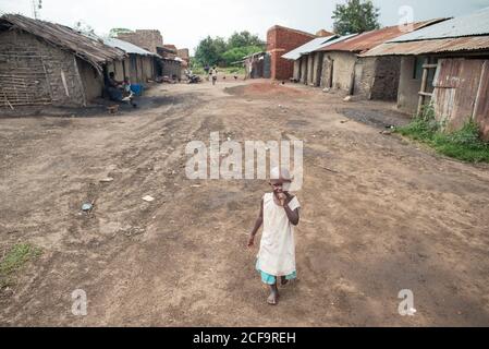 Uganda - Novembre, 26 2016: Da sopra il toddler africano calvo sorridente e meritare spuntino mentre camminando su strada sporca fuori dai baracche intemperie nel villaggio Foto Stock