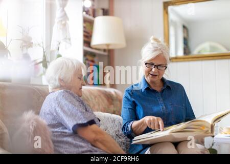 Donna anziana e sua figlia adulta guardando un album fotografico insieme sul divano in soggiorno Foto Stock