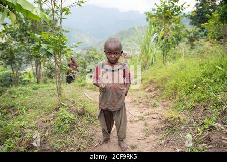 Uganda - Novembre 26 2016: Toddler africano calvo che guarda la macchina fotografica mentre cammina sulla strada sporca fuori del villaggio Foto Stock