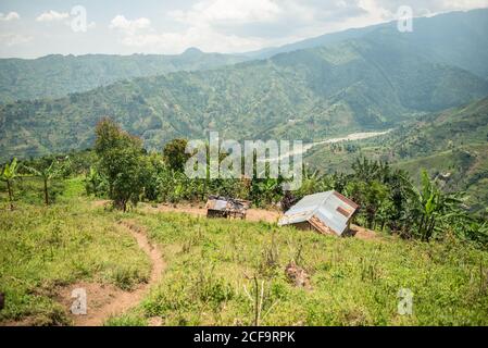 Uganda - 26 novembre 2016: Da sopra magnifico scenario di campagna con piccoli campi coltivati e villaggio solitario tra colline con verde erba lussureggiante e fitte foreste Foto Stock