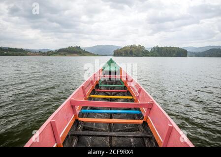 Uganda - 26 novembre 2016: Imbarcazione da pesca colorata in legno su un ampio fiume contro la pittoresca riva boschiva e l'altopiano nebbiato sotto il cielo nuvoloso grigio in luce naturale Foto Stock