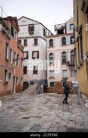 Vista laterale del viaggiatore in abiti caldi su ciottoli lastricati strada tra colorati edifici antichi in tempo nuvoloso in città via Foto Stock