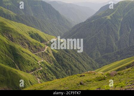 Dall'alto si può ammirare una splendida vista della strada a serpentina vuota sul verde Collina erbosa contro valle nebbiosa e montagne boscose in Georgia Foto Stock