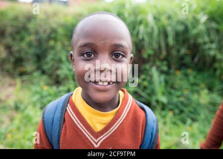 Uganda - Novembre 26 2016: Ragazzo africano calvo con uniforme da scuola guardando la macchina fotografica mentre si cammina sulla strada fuori dal villaggio Foto Stock
