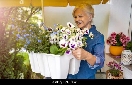 Donna anziana che si prende cura delle sue piante sul balcone Foto Stock