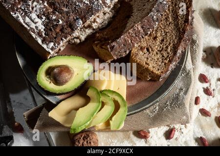 Vista dall'alto del pane integrale fresco a fette servito con avocado e formaggio per una sana colazione nutriente sul tavolo da cucina Foto Stock