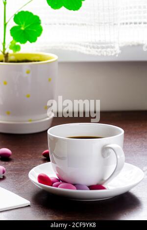 Un concetto accogliente. Una tazza di caffè con cioccolatini multicolore si trova su un tavolo di legno accanto a una pila di libri antichi Foto Stock