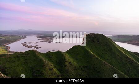 Verde collina erbosa in natura tranquilla vicino alle antiche rovine della torre con il paesaggio del lago sullo sfondo Foto Stock