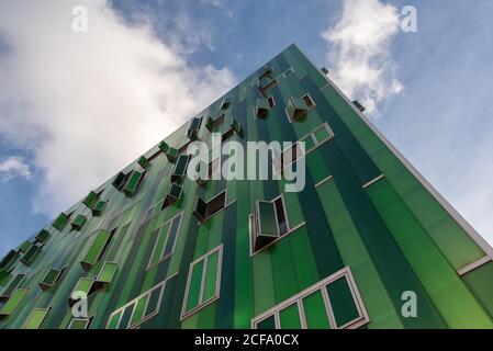 Dal basso si affaccia sulla facciata di un moderno edificio verde con finestre e pannelli a parete in una giornata di sole in città Foto Stock