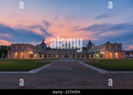 Facciata di palazzo medievale illuminato con vialetto e prati verdi sotto il cielo del tramonto Foto Stock