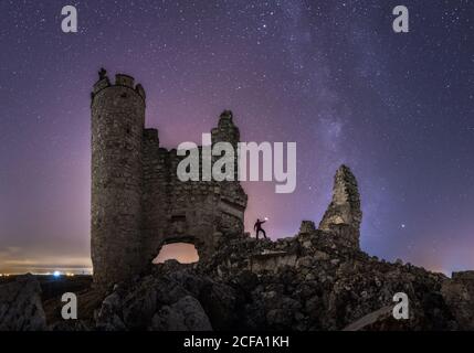 Da sotto vista posteriore di turista anonimo con lanterna esplorazione Rovinato vecchio castello sotto la Via Lattea nella notte stellata Foto Stock