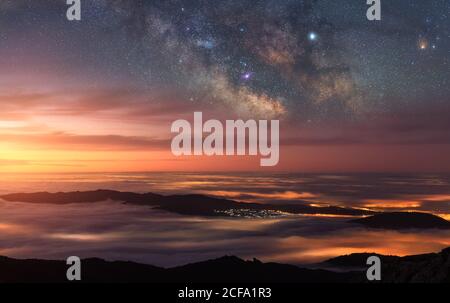 Vista sul drone di un'alba colorata mozzafiato che splende su una montagna scura picchi nelle nuvole sotto la luce delle stelle nella notte buia cielo Foto Stock