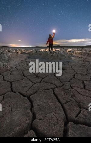 Silhouette di uomo irriconoscibile in piedi con torcia in mano maestoso scenario di terreno vulcanico con rocce porose e colorato Via Lattea sullo sfondo Foto Stock