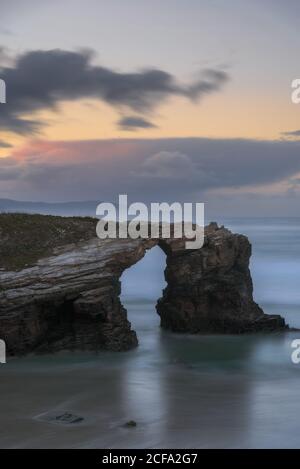 Grandi formazioni rocciose sulla spiaggia sabbiosa vuota dell'oceano con cielo nuvoloso e luminoso sullo sfondo Foto Stock