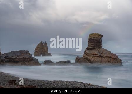 Grandi formazioni rocciose sulla spiaggia sabbiosa vuota dell'oceano con cielo nuvoloso e luminoso sullo sfondo Foto Stock