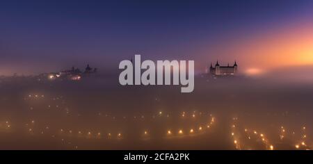 Dall'alto, si può ammirare un incredibile paesaggio di Alcazar e della città medievale illuminata De Toledo palazzo in nebbia colorata alba Foto Stock