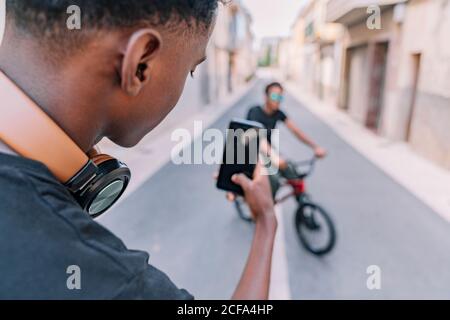 Da sopra raccolto messo a fuoco giovane ragazzo afro-americano che scattano foto su smartphone di maschio amico nero in bicicletta in strada Foto Stock