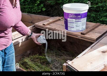 Donna che applica la calce ad un contenitore del composto o ad un mucchio del composto per contribuire a regolare l'acidità e ridurre gli odori. Foto Stock
