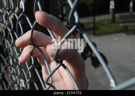 Mano maschio sulla recinzione della maglia della catena in posizione di parcheggio con le dita appeso al metallo Foto Stock