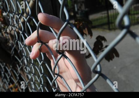 Mano maschio sulla recinzione della maglia della catena in posizione di parcheggio con le dita appeso al metallo Foto Stock