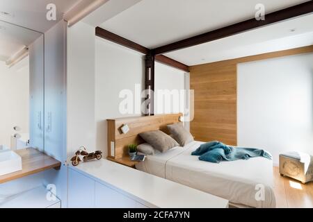 Interno di una camera da letto accogliente in un tranquillo stile minimalista e confortevole mobili in legno, pareti e soffitti bianchi Foto Stock