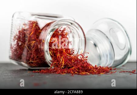 Closeup di zafferano aromatico naturale essiccato versato dal vaso di vetro posto sul tavolo Foto Stock